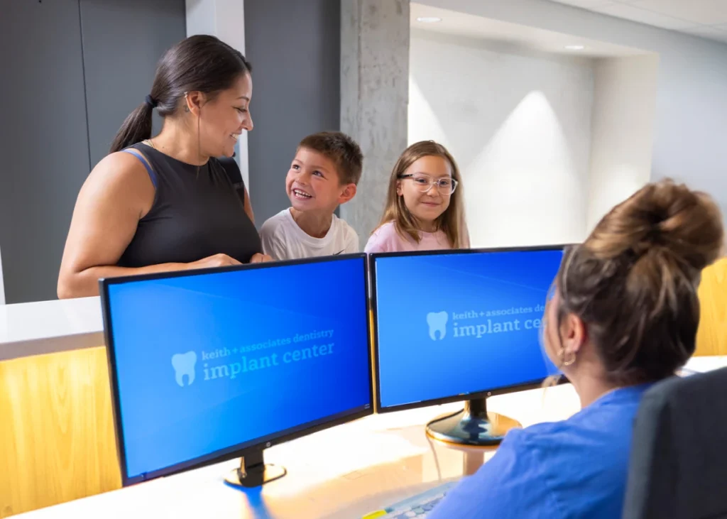 A mom with two children visiting the front desk of Keith and Associates Dentistry Implant Center.